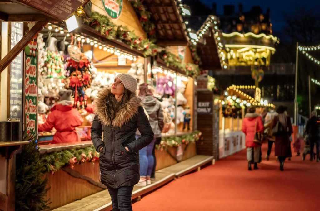 a woman in front of a bright stall at a Christmas market